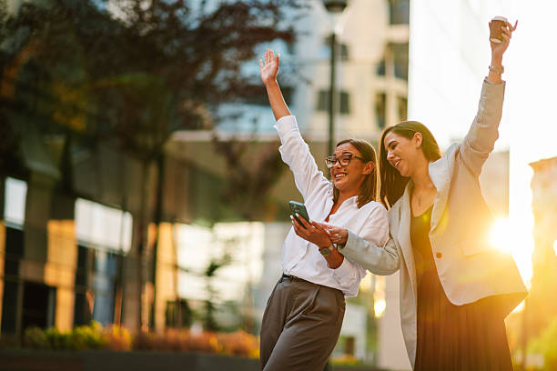 istock Two businesswomen celebrating success outdoors while looking at smartphone 2204634543