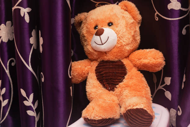 istock Brown children's teddy bear against purple curtains. 2204634789