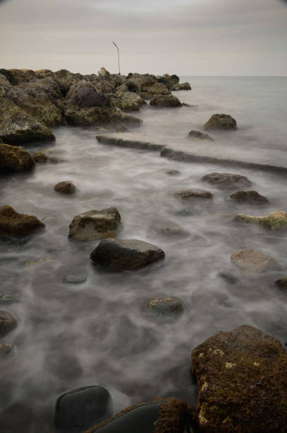 Soft waves gently lap against the rugged stones as twilight settles over the serene coastal landscape.