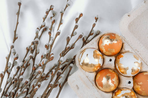 Gold Easter eggs in a carton  on a white silky background with willow branches. Easter  background.