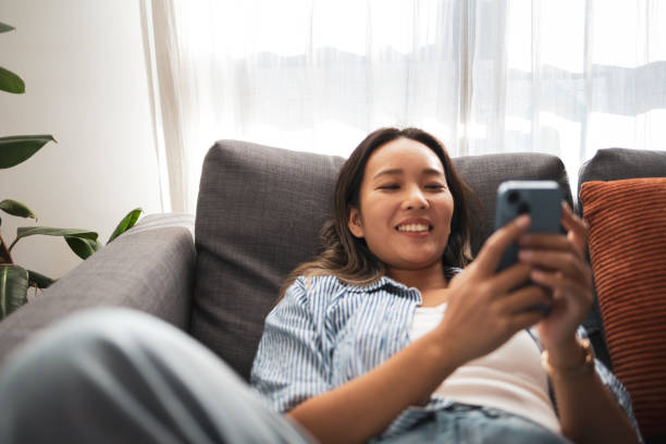 istock Young woman relaxing on a couch while using her smartphone 2204639975