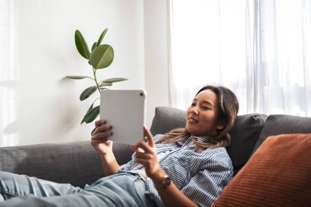 istock Asian woman relaxing on sofa with tablet in cozy home setting 2204640003