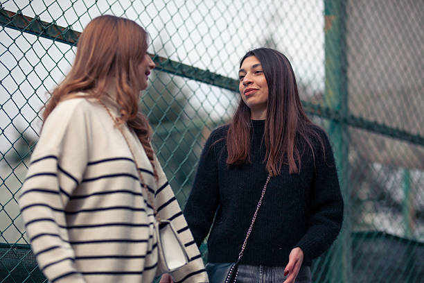 istock Two Young Women Having a Casual Conversation Outdoors Beside a Wire Fence 2204647762