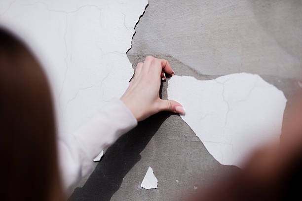 istock Close-up of a hand peeling cracked white paint from a damaged concrete wall surface 2204647912