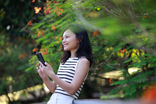 istock Asian Woman Using Smartphone in a Lush Green Park 2204649127