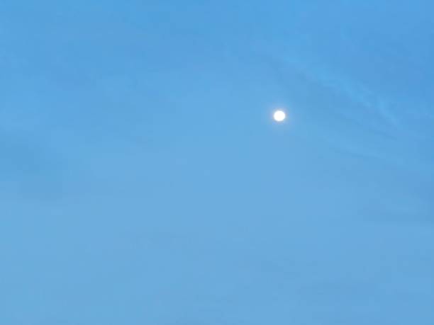 The evening blue sky has a pattern of faint clouds that create different shades of blue and the moon that is starting to rise has a soft yellow light.