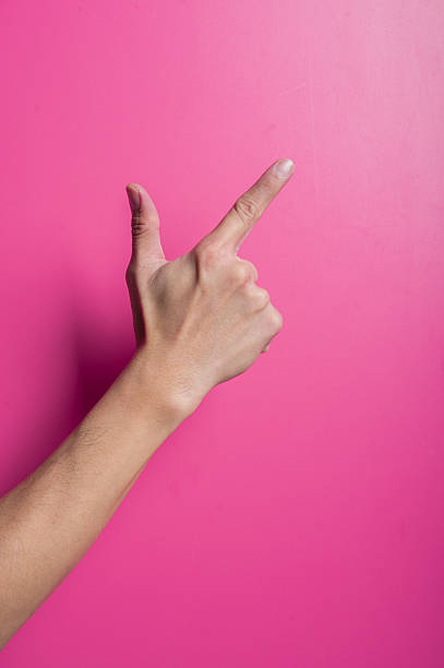 istock Asian hand forming a finger gun pointing sideways with thumb and index finger extended, isolated on pink background, symbolizing shoot, idea, target, or creativity. 2204657331