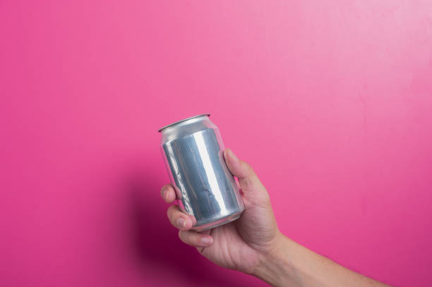 istock Asian hand holding a blank silver aluminum soda can against a solid pink background. The minimalist scene highlights beverage branding, advertising mockups, or refreshing drink concepts. 2204657564