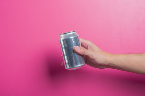 istock Asian hand holding a blank silver aluminum soda can against a solid pink background. The minimalist scene highlights beverage branding, advertising mockups, or refreshing drink concepts. 2204657612