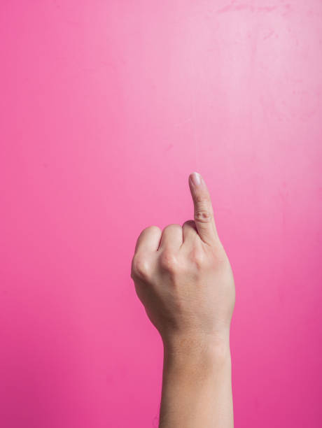 istock Asian hand raising one index finger upward while others remain curled, isolated against a bright pink background, commonly used to indicate attention, number one, or to emphasize a point. 2204657743