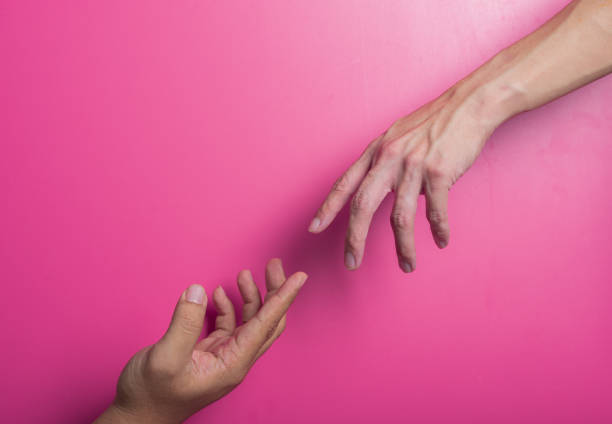 Two Asian hands reaching toward each other against a bright pink background, symbolizing connection, support, or human touch. Clean composition emphasizes emotion and interpersonal interaction.