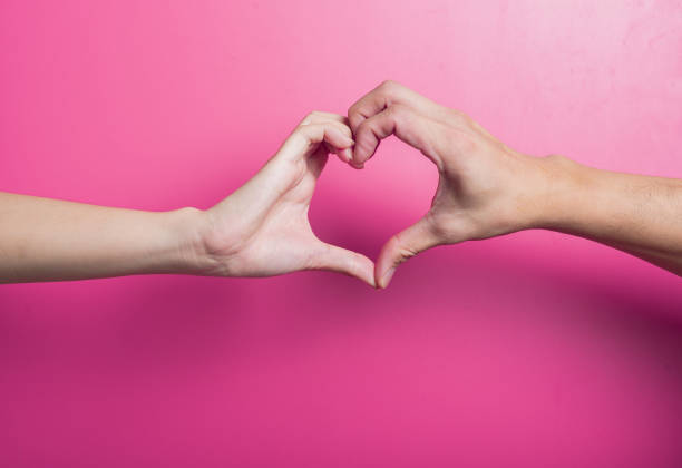 istock Two Asian hands forming a heart shape together against pink background, representing love, unity, care, and affection in a sweet and emotional gesture for romantic or social use. 2204659259