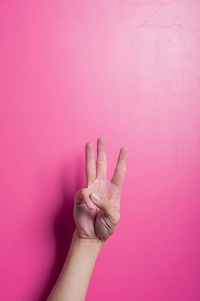 istock Asian hand showing the number three using index, middle, and ring fingers raised while thumb and pinky are folded, posed against a pink background with studio lighting for educational or symbolic use. 2204659730