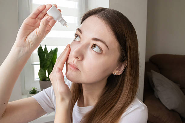 istock Woman holding eye dropper bottle and applying solution into her eye. Eye care routine. 2204663234