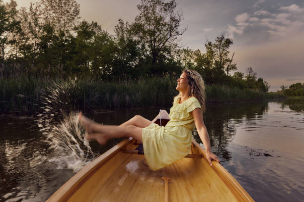 Happy woman having fun while splashing water with her leg from a canoe on a lake. Copy space.
