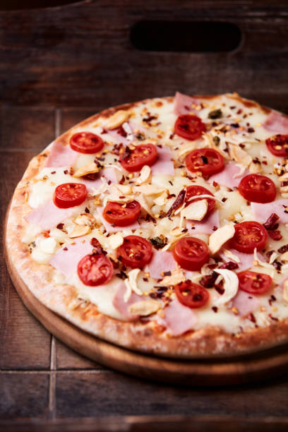istock Pizza with ham, cherry tomatoes and mozzarella cheese. Wooden background. Soft focus. Close up. 2204667516