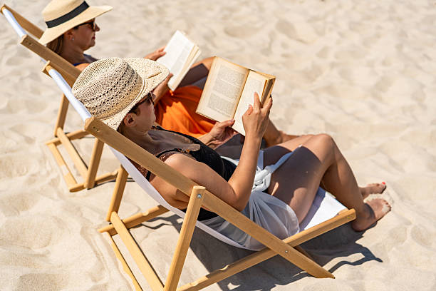istock Two mature women reading books sitting on deckchairs on beach 2204673574