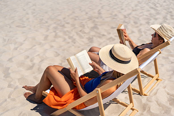 istock Two mature women reading books sitting on deckchairs on beach 2204673599