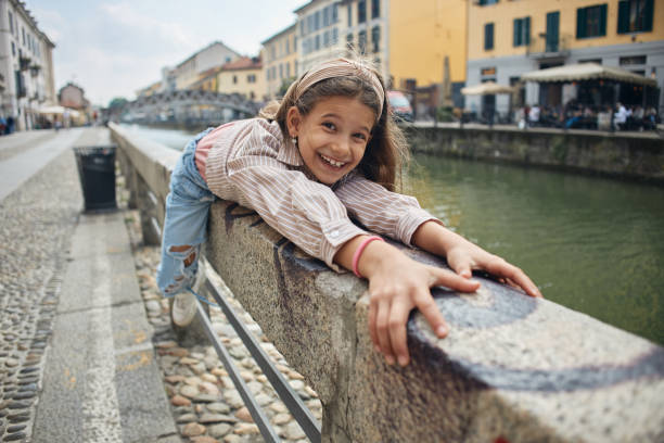 Little girl in white dress with long hair looks at the sea, stands on the parapet, looks at the mountains in the sunset light. Bright childhood filled with new discoveries. Family travel with children