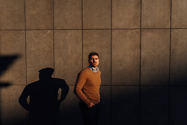 istock Businessman leaning against wall with shadow at sunset 2204677383