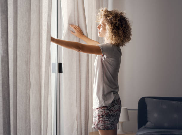 istock Young woman waking up and looking out the window 2204677516