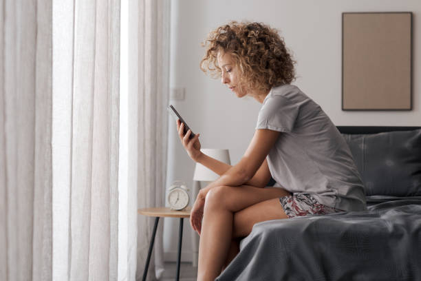 istock Woman sitting on her bed and checking her smartphone 2204677679