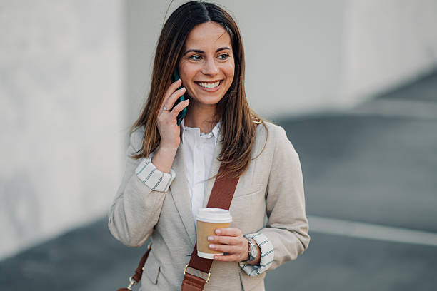 istock Smiling businesswoman walking and talking on phone while holding coffee 2204678467