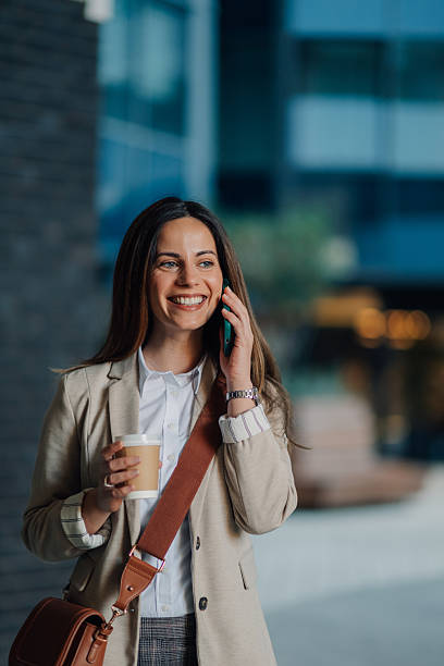 istock Smiling businesswoman walking and talking on phone while holding coffee 2204678500