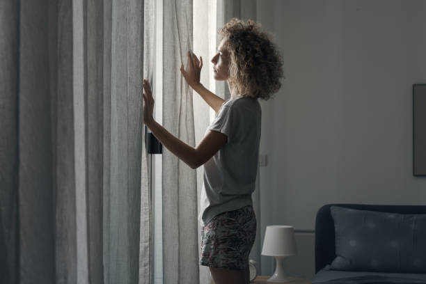 istock Young woman waking up and looking out the window 2204678522