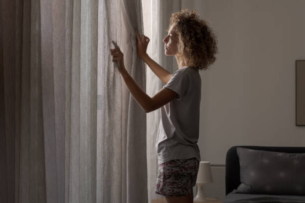 istock Young woman waking up and looking out the window 2204678549
