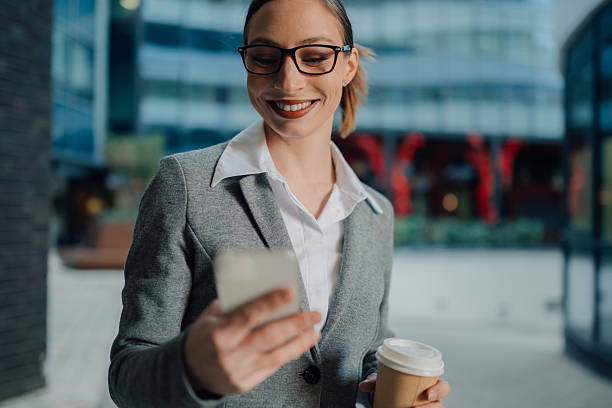 istock Smiling businesswoman using smartphone and holding coffee outside office 2204678556