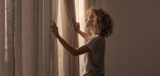 istock Young woman waking up and looking out the window 2204678715