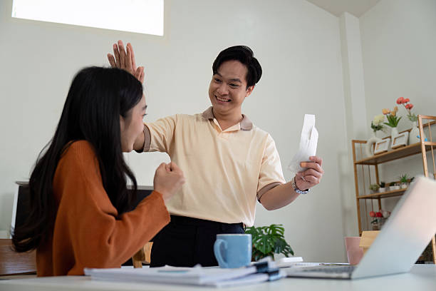 istock Couple celebrating financial progress. Young couple expressing joy while managing finances at home. 2204682510