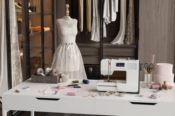 Tailor Studio. Mannequin With Wedding  Dress. Close-up Of Table With Sewing Machine, Threads, Tape Measure And Other Sewing Equipments