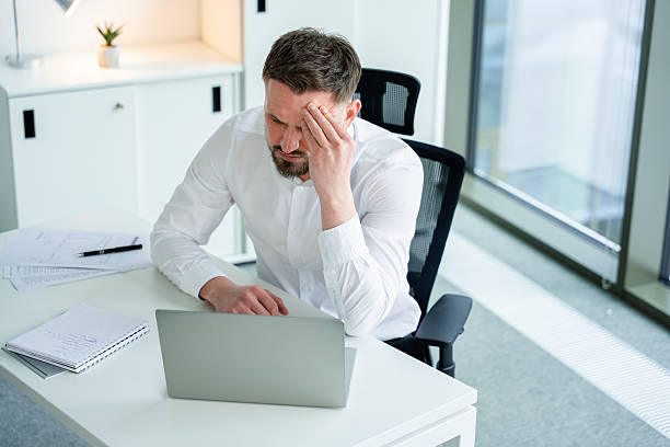 istock Frustrated Businessman in Modern Office Working on Laptop and Papers 2204690308