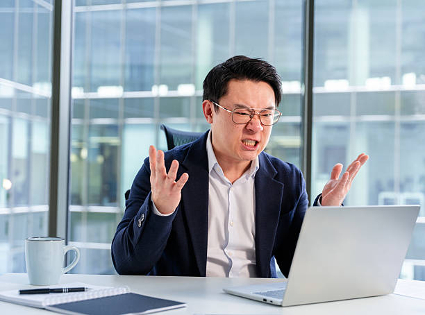 istock Frustrated Asian Businessman Expressing Stress While Working on a Laptop in Office 2204691976