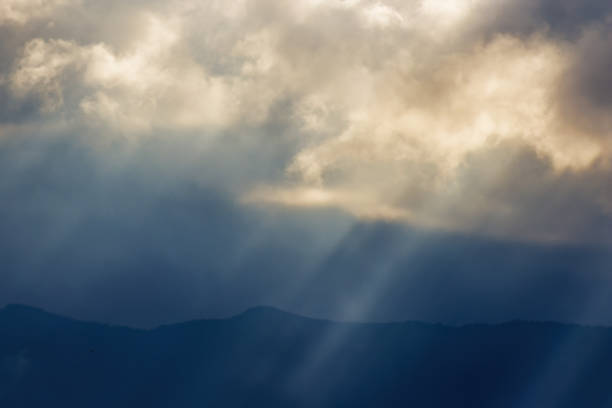 View of sunbeams going through dense dark clouds, in a rainy afternoon, over the eastern Andean mountains of central Colombia.
