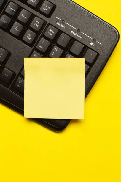 A blank yellow paper note on a black computer keyboard on a yellow background