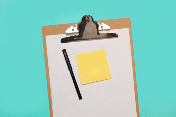 istock A blank yellow sticky paper and a black marker on a clipboard with white paper sheets on a light blue background 2204700968