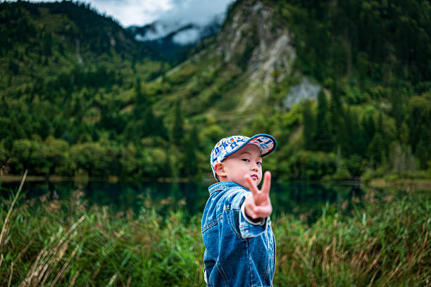 A boy stand on a wooden walkway by the lake in Jiuzhaigou. Distant green mountains reflect in the crystal-clear water, with mist swirling around, creating a poetic and picturesque scene