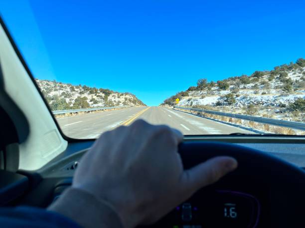 Hand holding steering wheel while driving along the iconic Route 66 in Arizona during winter, with a clear blue sky and snow-covered landscape