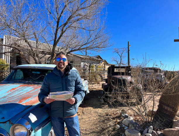 Tourist is holding a map in Hackberry, Arizona, a ghost town on Route 66, standing next to a vintage car wreck and other rusty vehicles, exploring the remnants of a bygone era