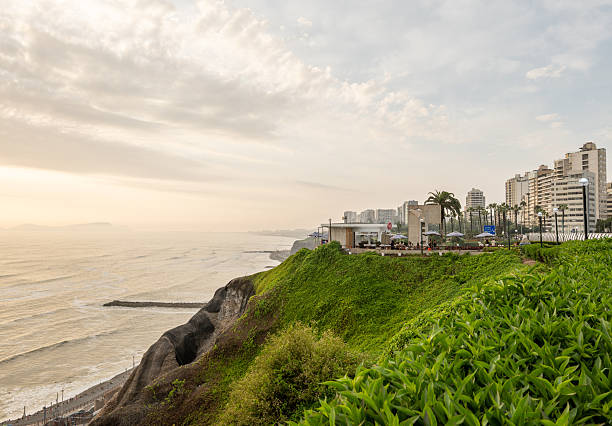 Scenic coastal landscape with lush greenery on cliffs and bustling city skyline. Coastal waves hit the shore beneath high-rise buildings. Ideal for urban planning and tourism.