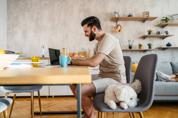 istock Young Man Working On A Laptop With His Dog Next To Him 2204709812