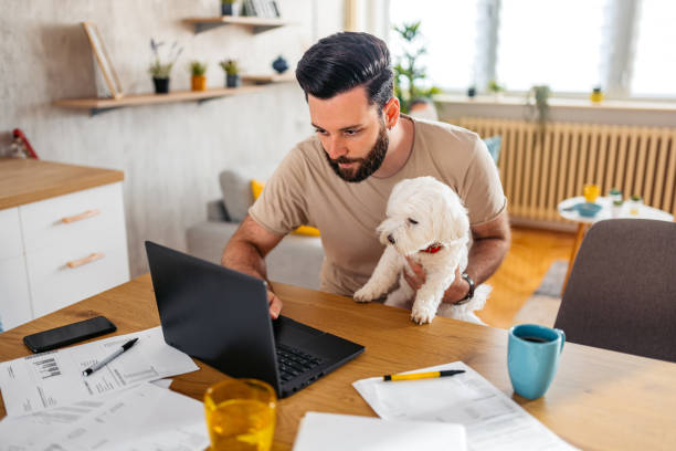 istock Young Man Working On A Laptop While Holding His Dog 2204711185