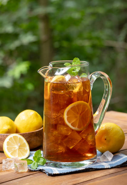 istock Pitcher of ice tea with lemon slices and mint outdoors on wooden table 2204712404