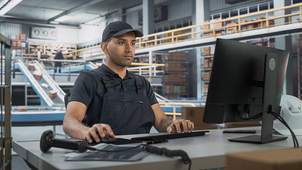 istock Multiethnic Male Manager Checking Inventory On Desktop Computer In Warehouse Facility With Conveyor Belt. Sorting Center Employees Carrying Boxes To Package Goods And Deliver To Clients. 2204712801