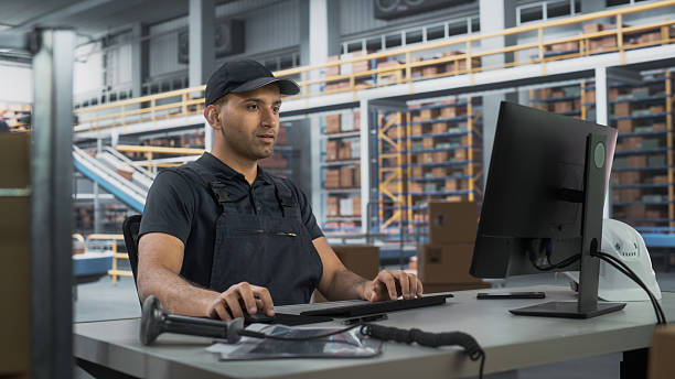 istock Multiethnic Male Manager Checking Inventory On Desktop Computer In Modern Warehouse Facility With Conveyor Belt. Sorting Center Employees Carrying Boxes To Package Goods And Deliver To Clients. 2204712822
