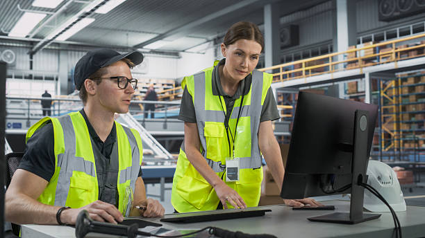 istock Caucasian Male Stocking Associate Talking to Female Manager And Using Desktop Computer In Warehouse Facility With Automated Conveyor Belt. Man And Woman Working In Sorting Center of Marketplace 2204712836