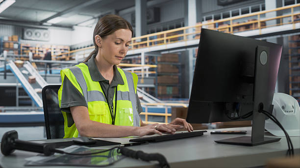 istock Caucasian Female Manager Checking Inventory On Desktop Computer In Warehouse Facility With Conveyor Belt. Sorting Center Employees Carrying Boxes To Package Goods And Deliver To Clients. 2204713265
